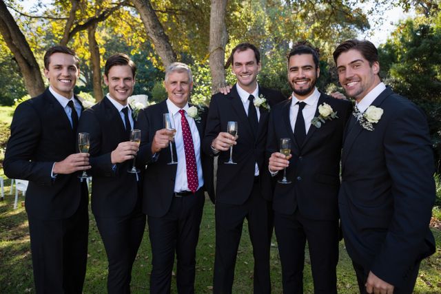 Portrait of groom and groomsmen having champagne in park