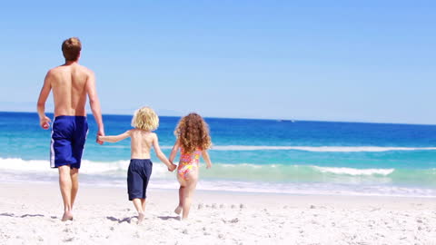 Father and Children Strolling by Ocean Shoreline on Sunny Day