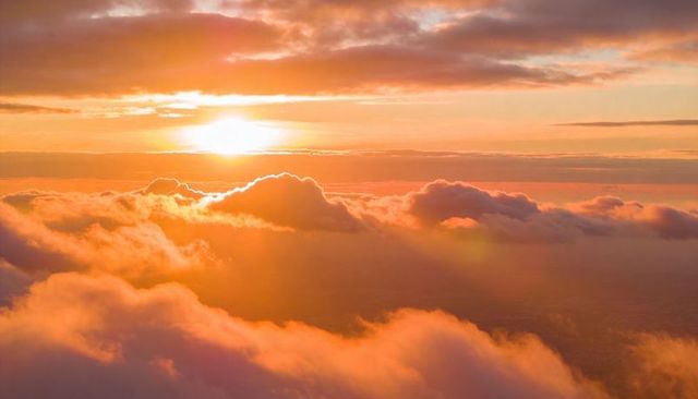 Aerial golden sunrise above cumulus clouds casting warm rays and sky glow