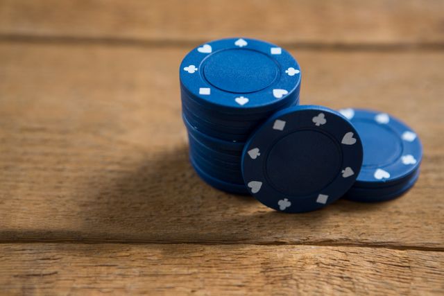Blue poker chips stacked on a wooden table, ideal for illustrating gambling, casino themes, or gaming activities. Perfect for use in articles, advertisements, or websites related to poker, betting, and leisure activities.