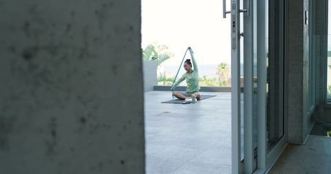 Woman stretching with resistance band on terrace overlooking ocean