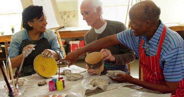 Three senior individuals participating in a pottery class, showcasing active engagement and collaboration. Ideal for promoting senior activities, community centers, art therapy, and the importance of creativity in later life. Perfect for content on senior inclusion, lifelong learning, and shared artistic experiences.
