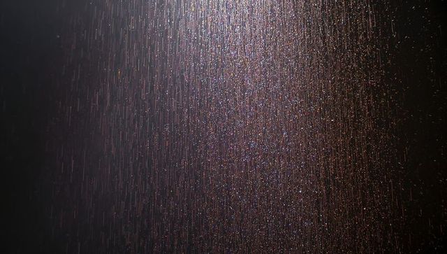 Iridescent rain streaks falling against dark night with soft upper-left light and bokeh