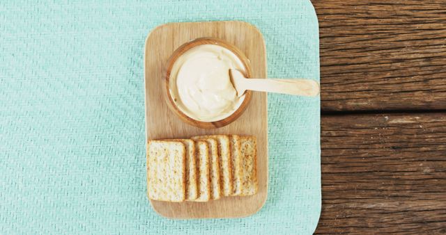 A wooden tray holds a bowl of dip with a spoon and slices of toasted bread on a turquoise cloth, with copy space. This setup is perfect for showcasing a simple and appetizing snack option.