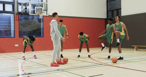 Basketball Coach Leading Warm-Up With Diverse Male Players in Gymnasium