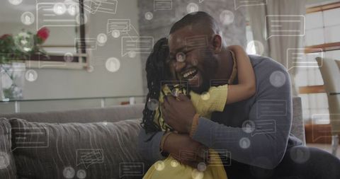 Black father and daughter hugging on sofa, laughing with social chat overlay