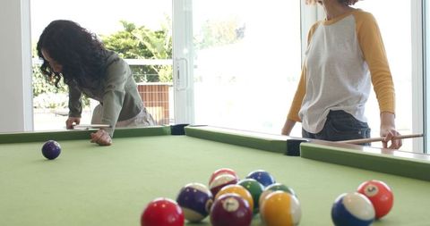 Female friends playing pool in sunlit patio room, casual social billiards moment