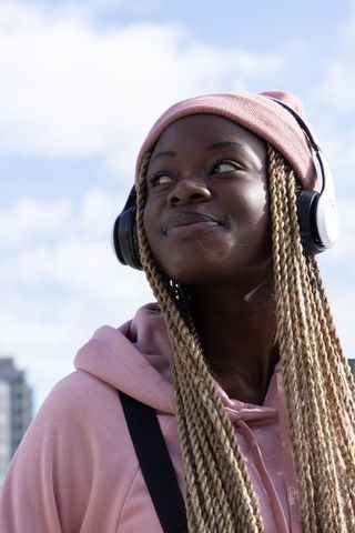 African American woman listening to music with headphones wearing pink beanie and braids