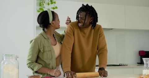 African american couple baking together in modern kitchen rolling dough and laughing, sharing warmth
