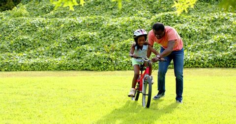 Father Teaching Daughter to Ride Bike Outdoors on Sunny Day