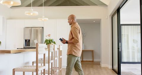 Mature man walking through modern open-plan kitchen holding smartphone by sliding door