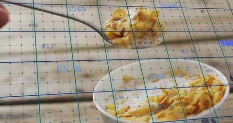 Spoon lifting cornflakes from milk bowl with teal digital grid overlay for food measurement