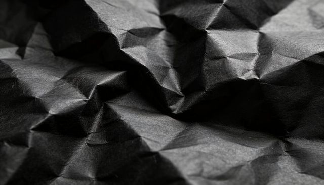 Crumpled black paper texture showing deep creases fibers and dramatic light contrast