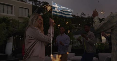 Friends Celebrating Outdoors at Night with Greek Flag and Sparklers