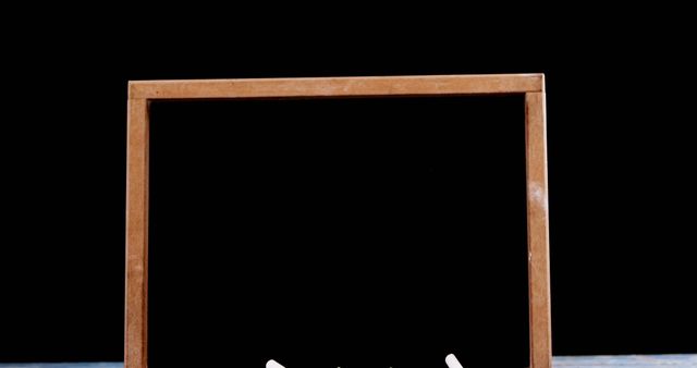 This picture showing a blank blackboard encased in a wooden frame, resting on a wood surface against a black background, is great for educational purposes, presentations, advertisements, and design projects. Its minimalist and neutral look makes it perfect for adding text, graphics, or educational messages to it. This blackboard can be an ideal visual aid for promoting educational content, classrooms decor, and teaching tools.