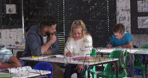 Teacher leaning in helping elementary student writing math notes while smiling