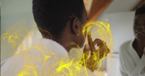 Man in bathrobe raising fingertip to forehead at mirror with golden particle glow