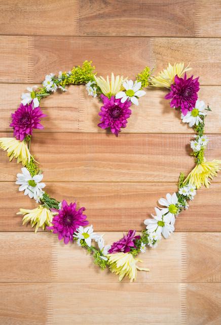 Tropical flower garland arranged in heart shape on wooden board, showcasing a vibrant and rustic touch. Ideal for use in romantic or love-themed projects, such as anniversaries, Valentine's Day, or wedding decorations. Also suitable for summer-themed events or as a cheerful, nature-inspired background for digital and print design.