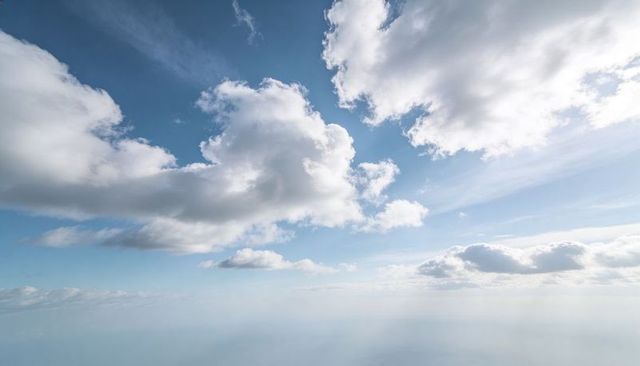 Floating cumulus clouds dominating bright blue sky over calm sea horizon and sun rays