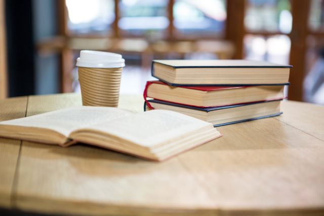 Close-up of books and disposable coffee cup on table in cafe