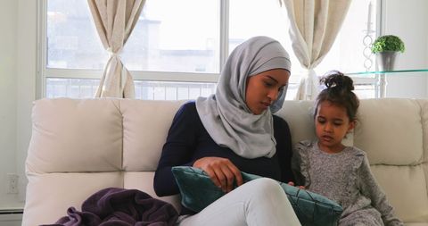 Mother with Hijab and Daughter Exploring Cushion Texture in Living Room
