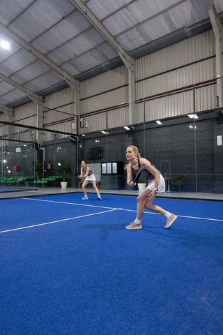 Female players playing padel doubles on indoor blue turf glass court in athletic action