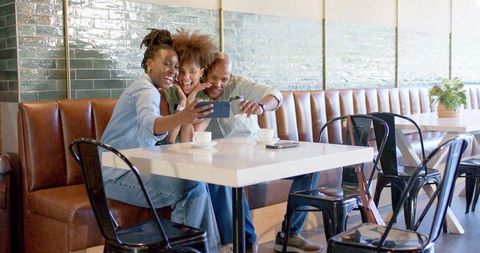 Friends taking joyful selfie at cafe booth with coffee cups and glossy subway tiles