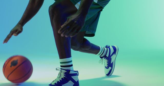 Image of midsection of african american male basketball player bouncing ball on blue background. Sports and competition concept.