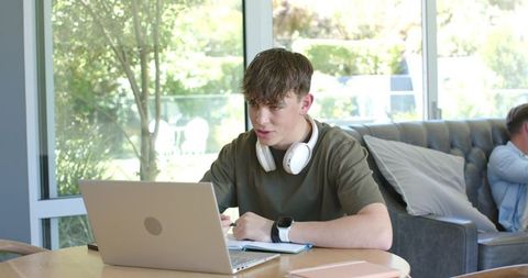 Teenager studying at home wearing headphones using laptop for remote learning success