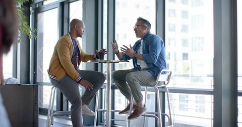 Black and white coworkers meeting over coffee and smartphones at modern office lounge