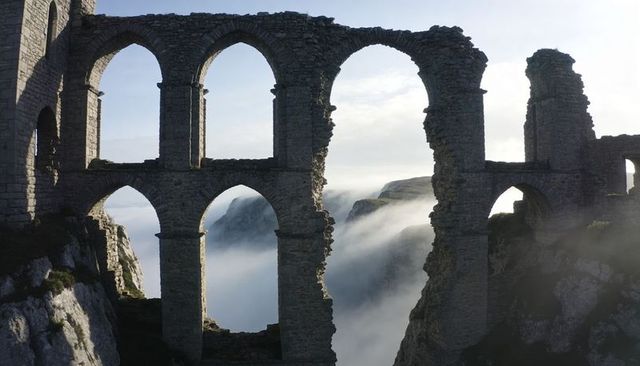 Crumbling stone arches overlooking fog-shrouded coastal precipice, atmospheric ruins