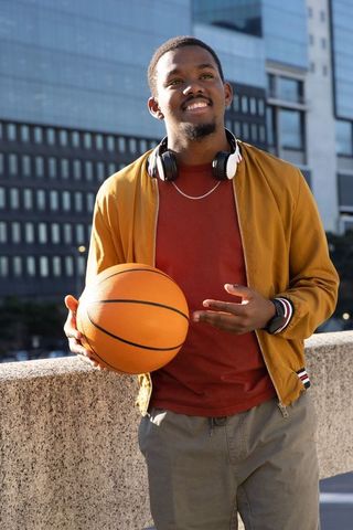 Smiling african american man holding basketball on rooftop wearing headphones