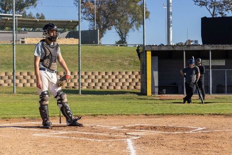 Youth Baseball Catcher Standing Ready at Home Plate with Teammates in Dugout