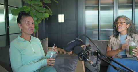 Two hosts recording podcast conversation in cozy minimalist studio with smoothies