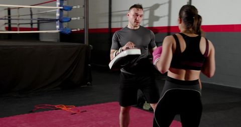 Male trainer holding focus pad while female trainee throwing punch with pink boxing gloves
