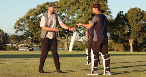 Coach demonstrating batting stance to young players on cricket field at golden hour