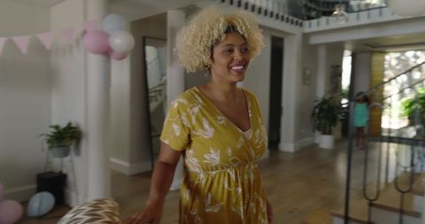 Smiling woman wearing mustard-yellow floral dress welcoming guests at home party