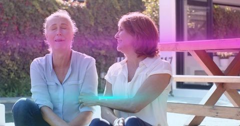 Mature women comforting each other on sunlit patio showing support and friendship