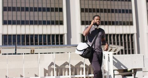 African american man leaning on terrace railing talking on phone with gym duffel in city