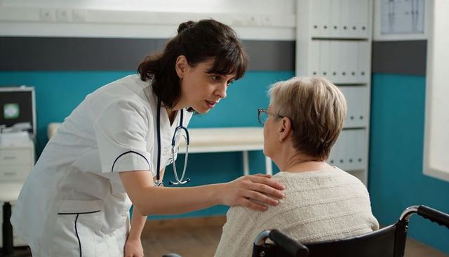Nurse comforting senior woman in wheelchair during clinical consultation, showing empathy