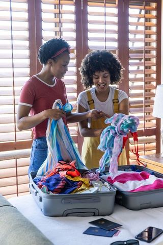 African american friends packing swimwear for sunny vacation in bedroom with shutters
