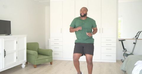 African american man jogging in place in bright minimal bedroom home gym with headphones