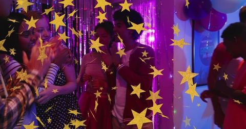 Friends clapping hugging and holding cups at neon party with metallic fringe and balloons