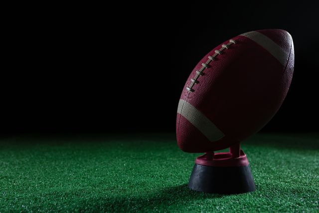 Close-up of American football standing on holder on artificial turf against black background