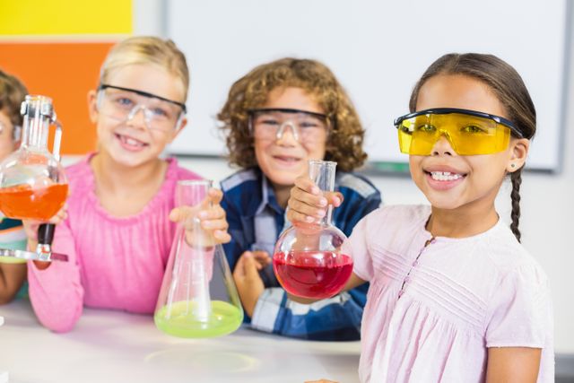 Children conducting a chemistry experiment in a classroom, wearing safety goggles and holding beakers with colorful liquids. Ideal for educational materials, science-related content, school projects, and promoting STEM education.