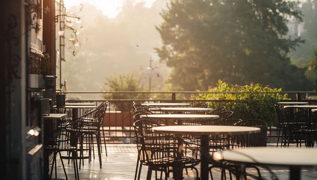 Sunlit empty cafe terrace with round metal tables and wire-frame chairs at golden hour