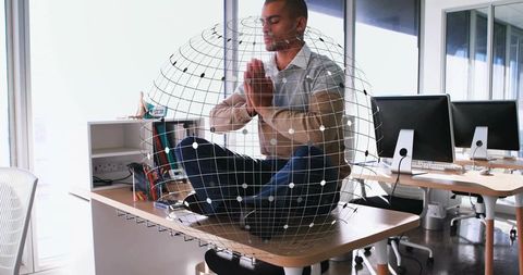 Man meditating on desk with digital globe overlay in bright open-plan office