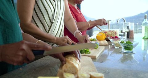 African american mature and senior women preparing salad and slicing baguette on kitchen island
