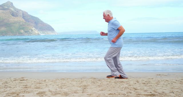 A senior Caucasian man is jogging on a sandy beach near the ocean, with copy space. His active lifestyle exemplifies the importance of physical fitness in maintaining health and vitality in later years.