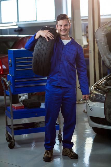 Portrait of mechanic carrying a tyre in repair garage